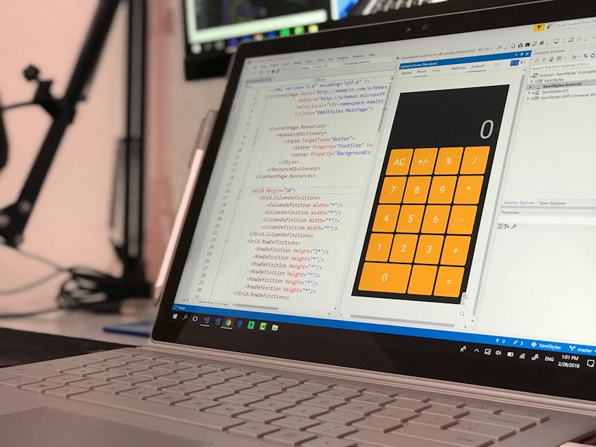 A person with light skin is using a slim, modern laptop with a silver exterior, placed on a dark surface. The laptop's screen displays a dark-themed coding or programming interface, featuring lines of